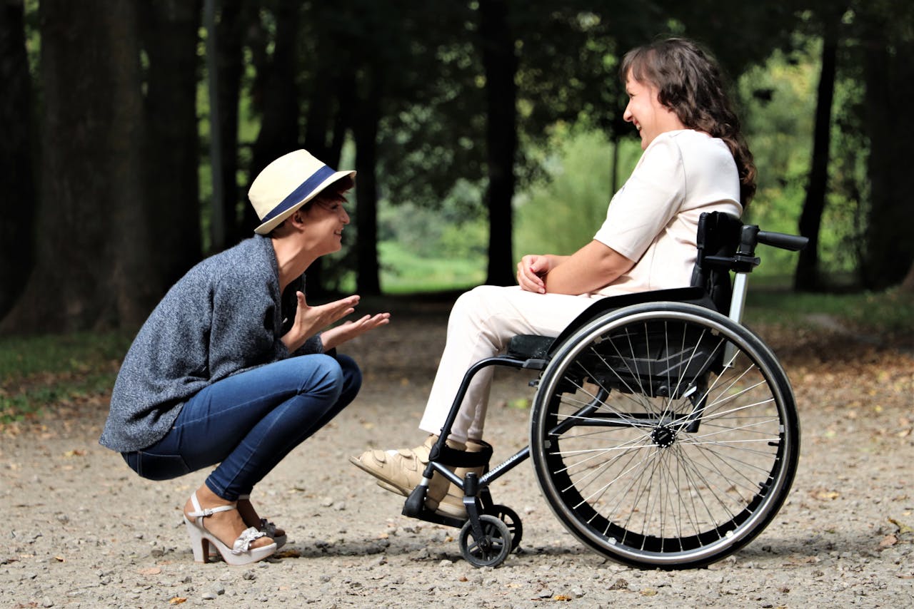 Two young women chatting in a park, one using a wheelchair
